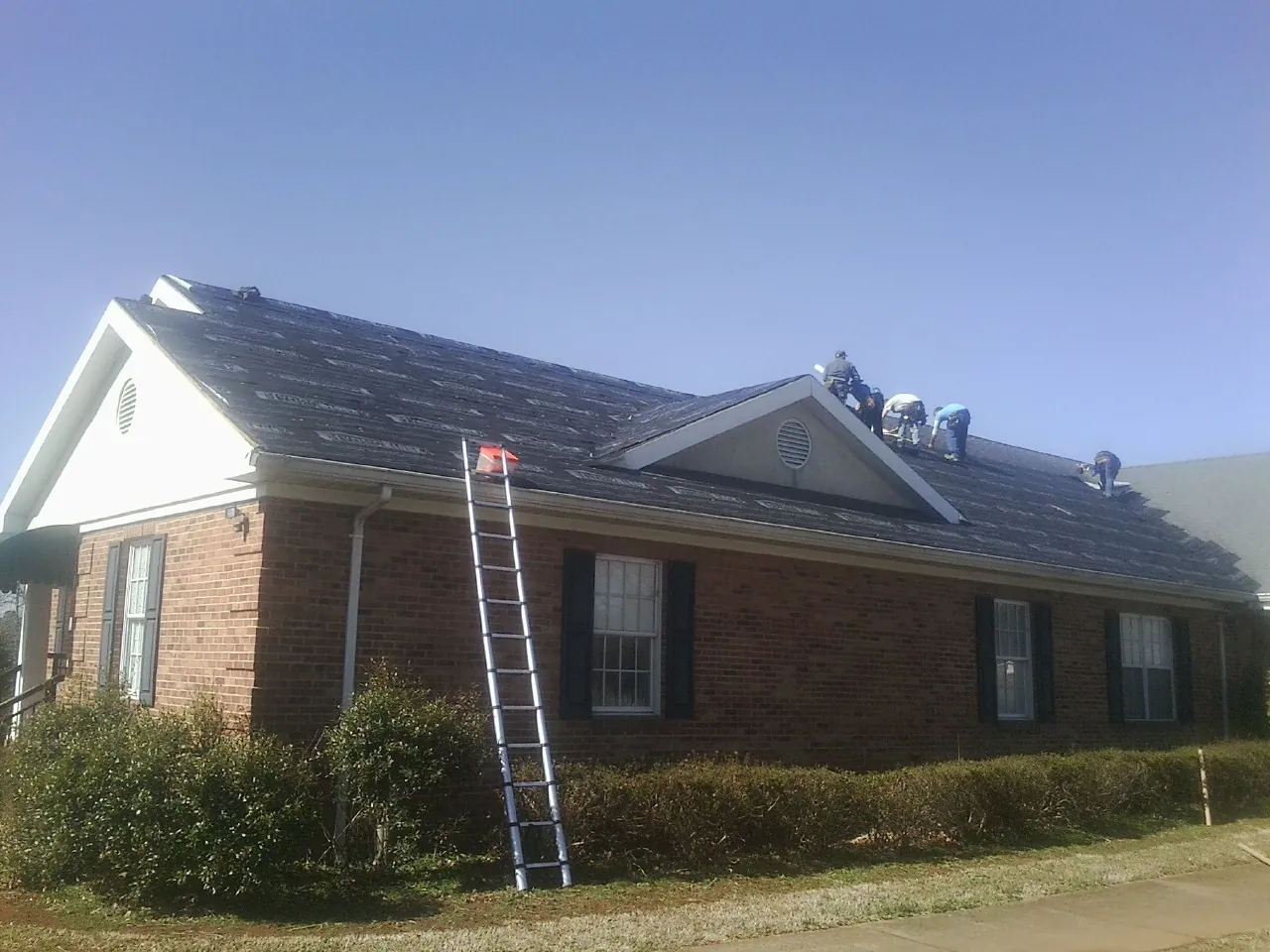 Crew tearing shingles off a brick ranch roof with a ladder set — Emergency Roof Repair work by our crew in Clairfield