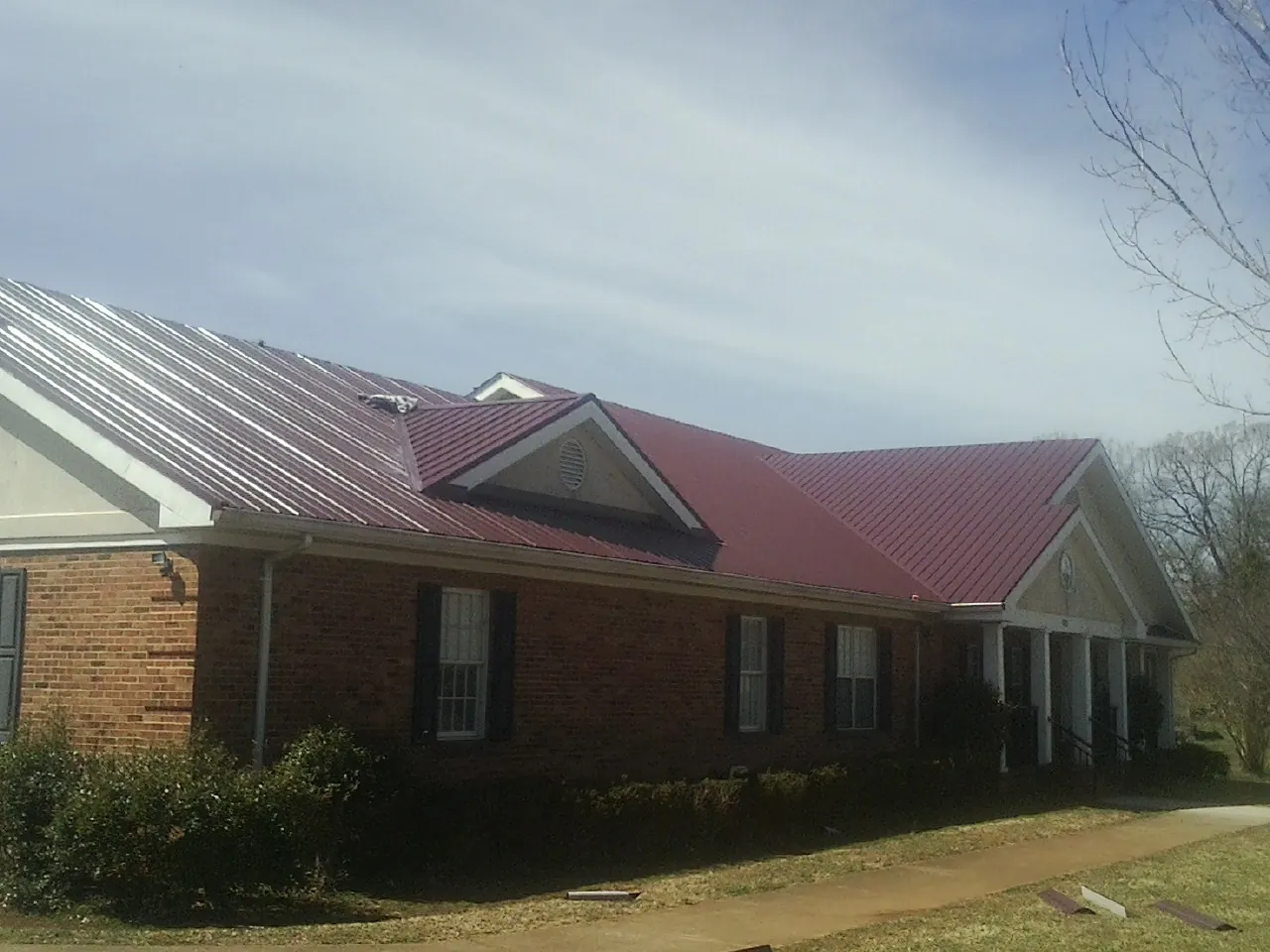 Red metal roof with gabled entries on a long brick building, from a Hail Damage Roof Repair job in Clairfield