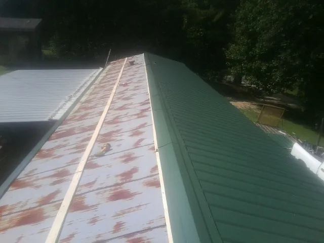Old rusted panels beside newly installed green metal roofing — Wind Damage Roof Repair by Roofing Brothers in Clairfield