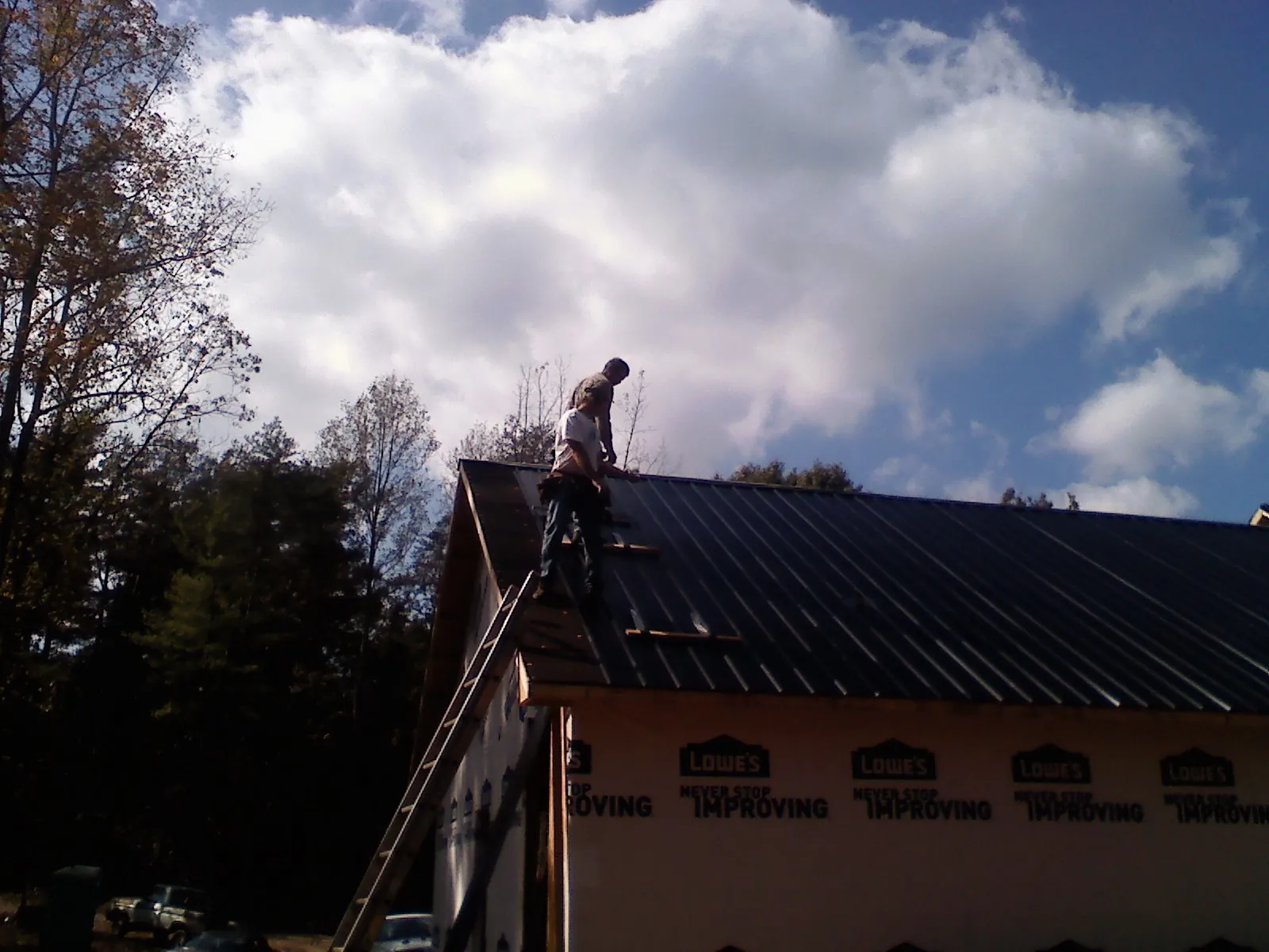 Roofer fastening dark metal panels high against a cloudy sky, from a Roof Inspection job in Clairfield